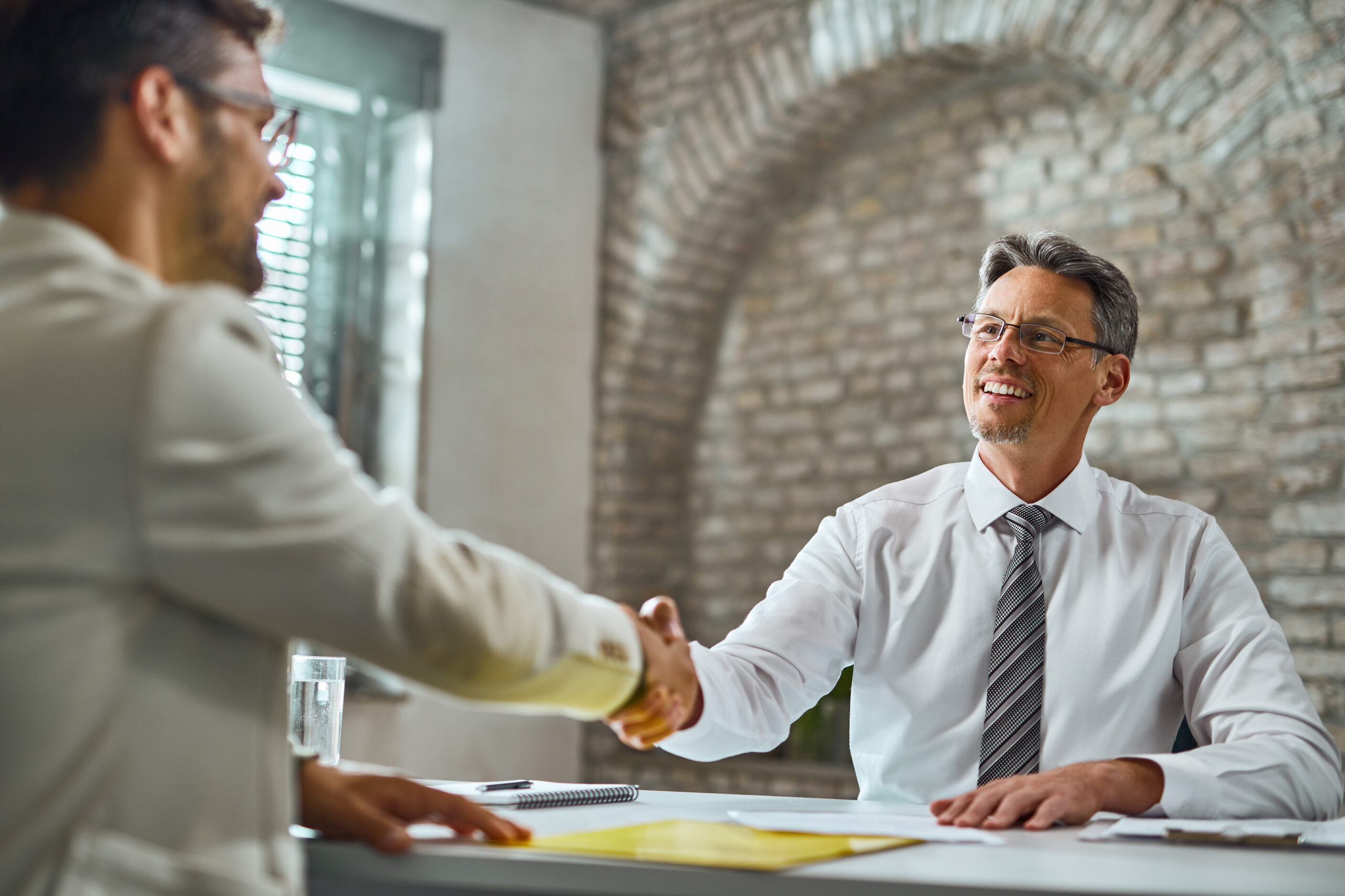 Happy manager handshaking with a candidate after successful job interview in the office.