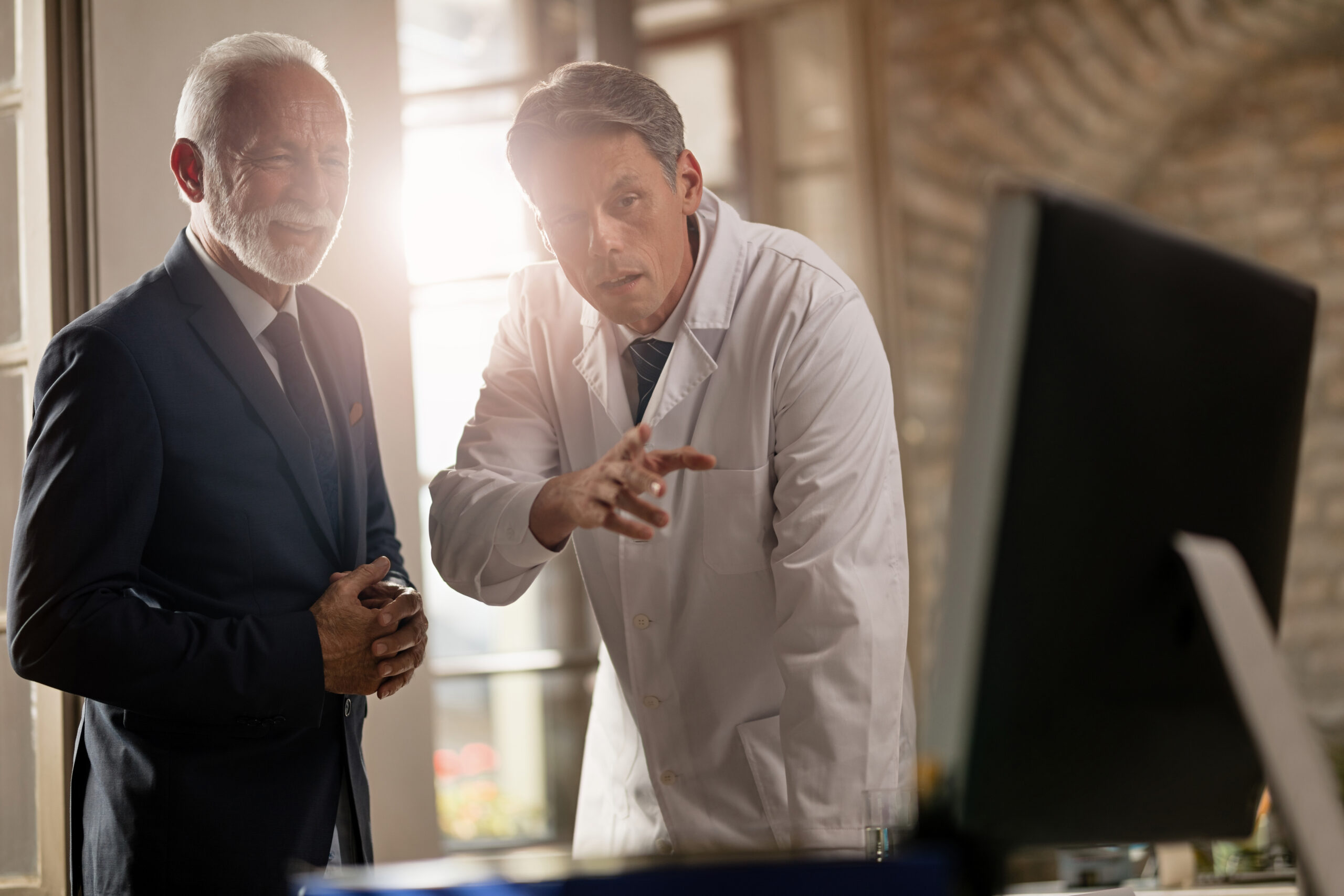 Mid adult doctor explaining to mature businessman medical data on a computer at clinic.