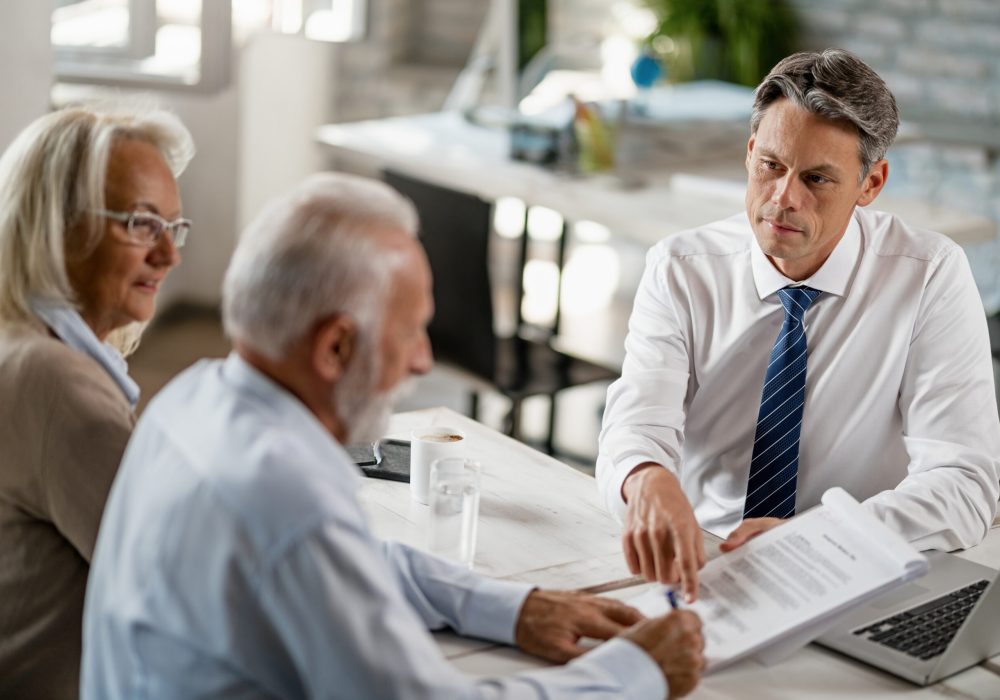 Bank manager having a meeting with senior couple and pointing at place they need to sign on the contract.