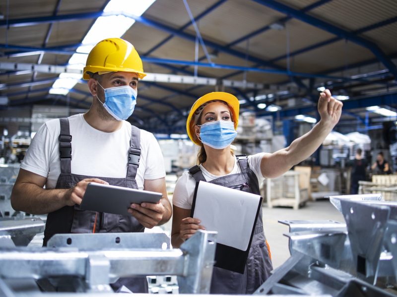 Factory workers with face masks protected against corona virus doing quality control of production in factory.