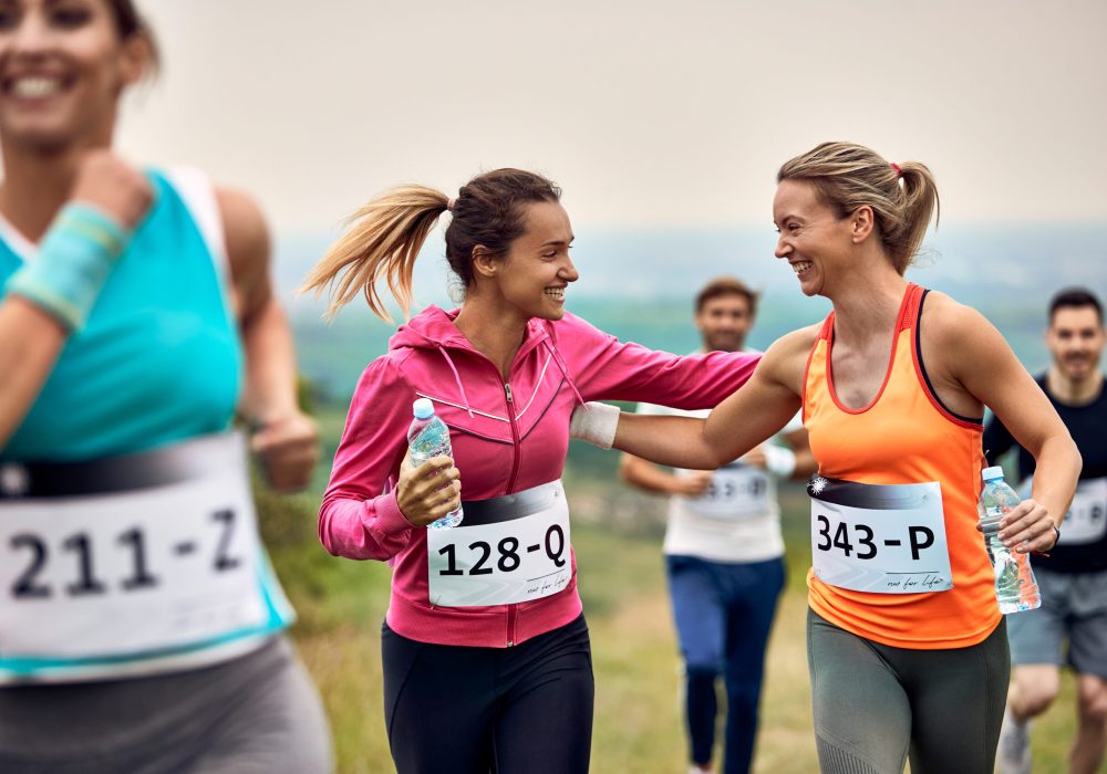 Happy athletic women supporting each other while running a marathon in nature.