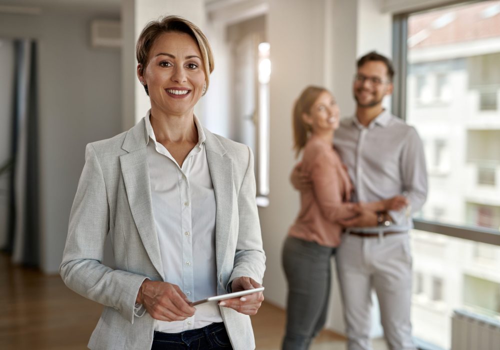 Portrait of female real estate agent looking at the camera while happy couple in standing in the background.