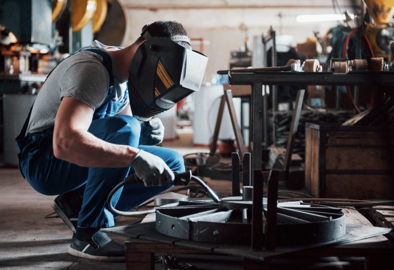 Portrait of a young worker at a large metalworking plant. The welder engineer works in a protective mask.